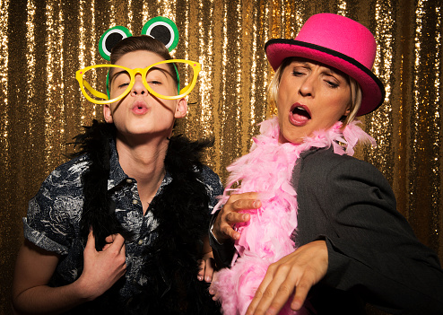 Portrait of cheerful male and female friends wearing party props and taking photos at photo booth during the party.