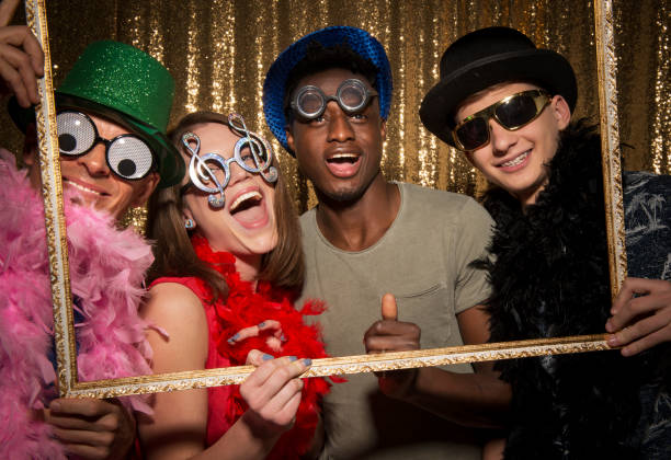 Male and female friends enjoying party Portrait of cheerful male and female friends wearing party props and holding picture frame while taking funny photo at photo booth during the party. Boa stock pictures, royalty-free photos & images