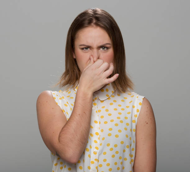 Close-up of young woman holding nose Portrait of beautiful young woman holding nose while standing against grey background. holding nose stock pictures, royalty-free photos & images
