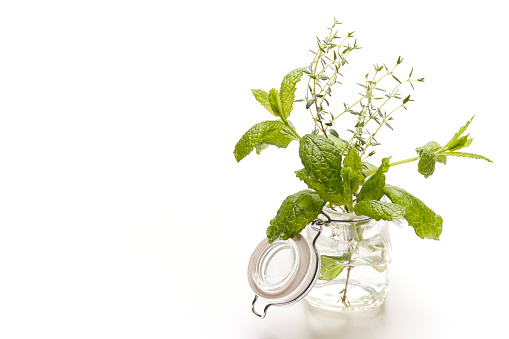 Thyme and lemon balm leaves in a glass pot on a white background.
