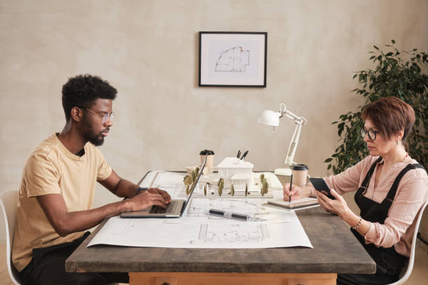 istock Multi-ethnic construction sales managers sitting against each other in office and working with customer online using devices 1322371040