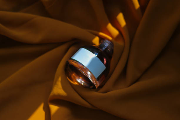 istock Perfume bottle with blank white label and light and shadow contrast on textured orange fabric background. Perfume bottle stock photo 1322374934