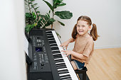 Perky little girl showing off, playing electric piano at home. High angle.