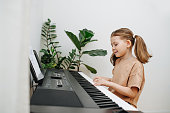 Keen little girl makes effort playing electric piano at home. Side view.