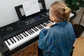 Attentive little boy is learning to play electric piano at home. From behind.
