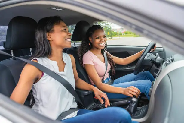 Photo of Young black teenage driver seated in her new car with her mother
