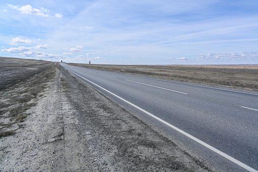 Highway road in the steppes, bushes, grass and cloudy sky. Spring landscape.