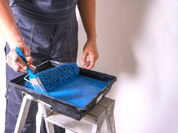 istock The painter dips his brush in paint bath of blue paint. Cuvette for rollers on a stepladder. 1322379909