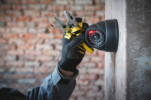 Security camera on the wall close up and worker hand with a work tools. Video surveillance system maintenance concept.