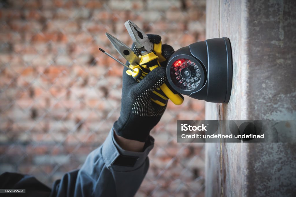 Security camera. Security camera on the wall close up and worker hand with a work tools. Video surveillance system maintenance concept. Security Camera Stock Photo