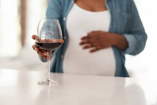 gros plan d’une femme enceinte tenant un verre de vin rouge à la maison - abdomen addiction adult alcohol photos et images de collection