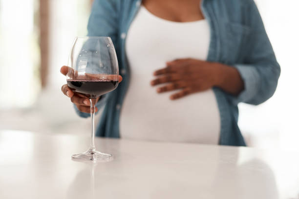 colpo ravvicinato di una donna incinta che tiene in casa un bicchiere di vino rosso - abdomen addiction adult alcohol foto e immagini stock