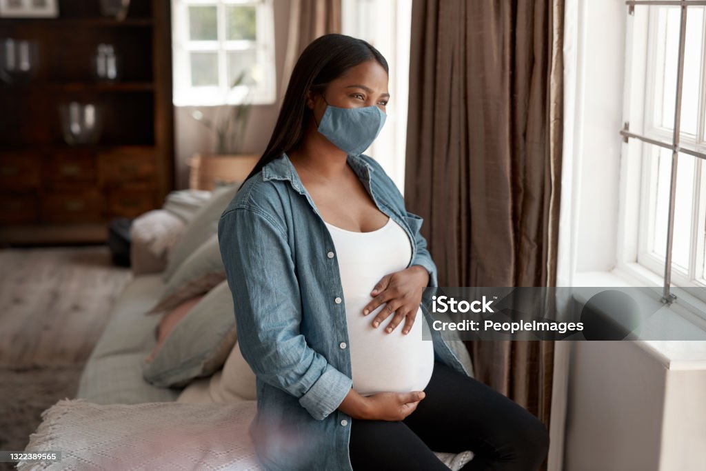 Shot of a pregnant woman wearing a face mask and looking thoughtful at home Pregnancy has been a challenging experience through the pandemic Pregnant Stock Photo