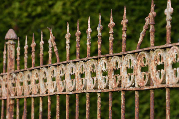 An old weathered metal fence with peeling paint against a green background An old weathered metal fence with peeling paint against a green background rusty fence stock pictures, royalty-free photos & images
