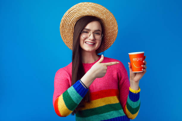 Young girl with eyeglasses points at takeaway coffee, has joyful expression