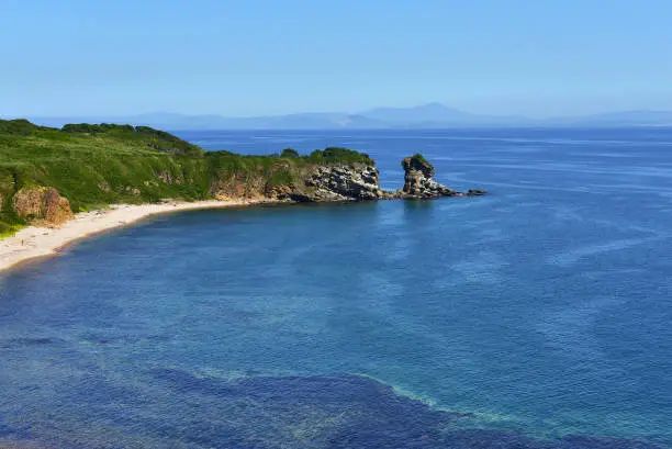Mountains and seascape with blue sky. Green vegetation in the mountains, sandy beach and amazig sea.