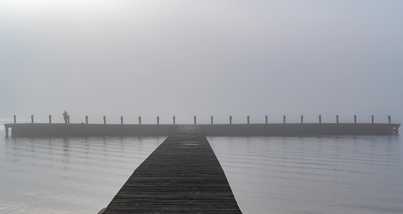 A man fishing off the pier in the morning fog.