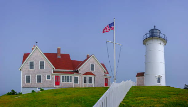 Panoramic view of the white lighthouse and red roof house over the fresh flowerily green hill on a bright sunny day in springtime in Woods Hole, Massachusetts.