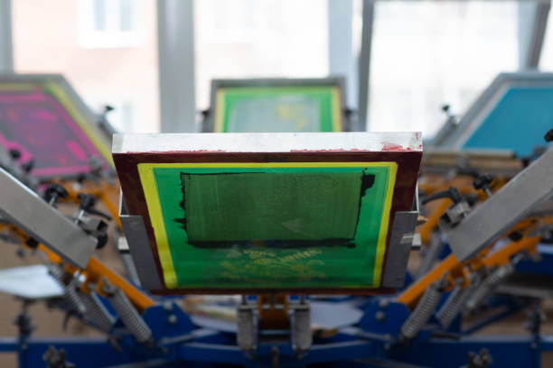 istock Carousel Frame, squeegee and plastisol color paint Serigraphy silk screen print process at clothes factory. 1322414441