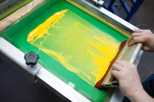istock Serigraphy silk screen print process at clothes factory. Frame, squeegee and plastisol color paints 1322414442