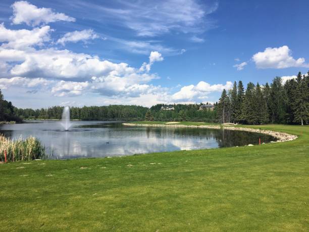 A beautiful view of a par 4 golf hole surrounded by a giant lake and a fountain.The scenic hole requires an approach shot over the water and is also surrounded by forest. In Innisfail, Alberta, Canada stock photo
