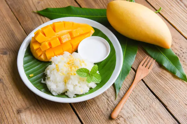 Ripe mango rice cooked with coconut milk, Sticky rice summer tropical fruit food Asian Thai dessert sweet mango peel and sliced on banana leaf and fresh mint leaves