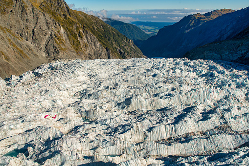 Looking down to the dramatic ice floor of the Southern alps glacier with a red helicopter flying below