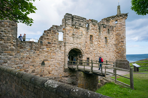 St. Andrews, Scotland, UK - June 20, 2019: Tourists walk across the wooden walkway over the moat to reach St. Andrews Castle, Scotland, Fife coast, UK
