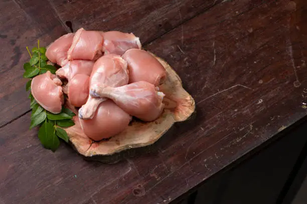 Raw chicken cuts or parts  like breast fillet,chicken stripes; chicken legs without skin arranged on a sliced wooden log base and garnished with curry leaves and placed on wooden background