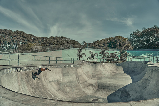 skateboarder on rollerskates jumping in a grey skatepark, shades of green image.
