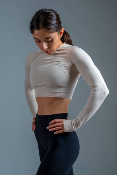 istock Young sportswoman standing akimbo with head down on grey background 1322439663