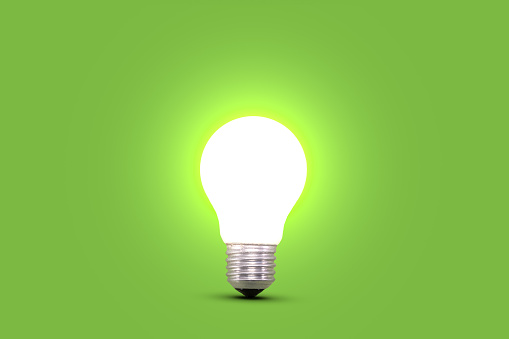 One illuminated energy saving light bulb on green background. Side view. Glowing lamp bulb. Concept for ideas, innovation and savings.