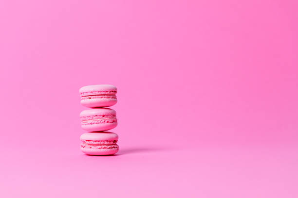Three pink macaroons with pink filling stacked on pink background