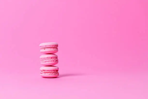Three pink macaroons with pink filling, on top of each other on pink background, studio shot