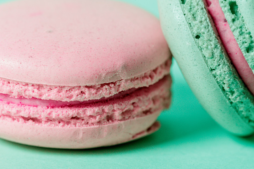 Close-up on rose colored macaroon with rose filling and mint green one leaning on it, mint background, studio shot