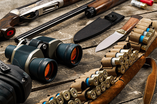 Hunting equipment set on old wooden background including rifle, knife, binoculars and cartridges