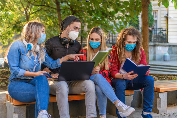 istock Handsome Group of Students in Shirts is Working on a Laptop in a Park with Protective Masks. 1322454598
