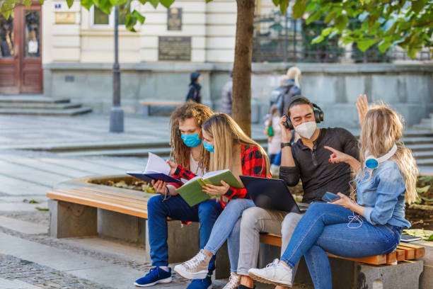 istock Beautiful Students are Working on a Laptop in Public Park with Preventive Measures due to Coronavirus. 1322454800