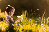 Cute little girl making bubbles from bubble gun in springtime.