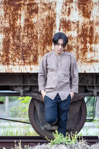 Photo of Portrait Of Smiling Handsome Asian Man Standing At Public Train Station. Young Man Standing In Old