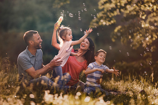Happy parents and their small kids having fun while making bubbles during spring day in nature.