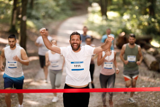 успешный марафонец пересекает финишную черту с поднятыми руками. - marathon jogging running finishing стоковые фото и изображения