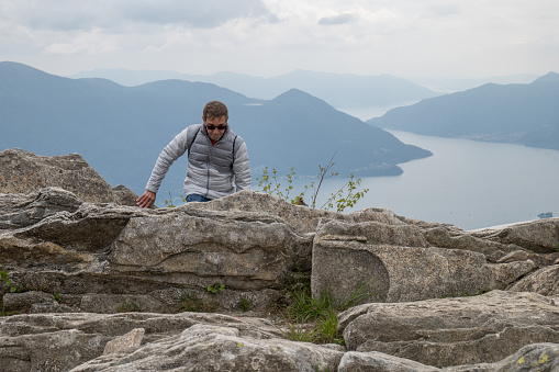 He climbs on rocks, lake on background. Ticino