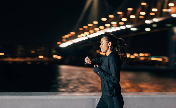 young middle east woman jogging at night looking in fitness tracker on her wrist - night running imagens e fotografias de stock