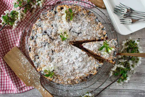 fresh and homemade baked rustic cherry crumble cake from Germany served on a cooling rack with forks and plates on white wooden table background. Overhead and isolated view