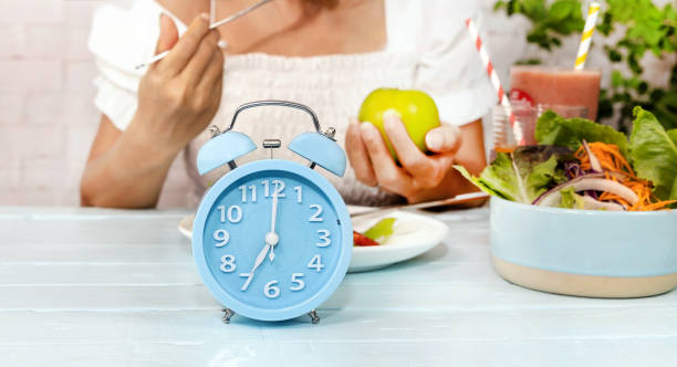 istock Selective focus of blue clock  which young woman Intermittent fasting eating  tomato as salad  of healthy food concept image in the kitchen room 1322467321