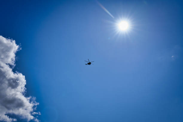 Silhouette of a helicopter against a blue sky with clouds