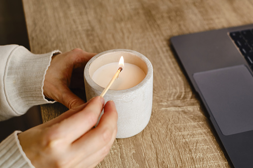 The girl lights a candle at her desk at home. A minute of relaxation after working with a laptop. Relaxation and Zen atmosphere