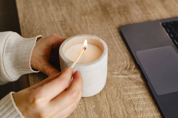 a garota acende uma vela em sua mesa em casa. um minuto de relaxamento depois de trabalhar com um laptop. relaxamento e atmosfera zen - vela equipamento de iluminação - fotografias e filmes do acervo