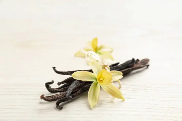 Beautiful vanilla flowers and sticks on white wooden table, closeup